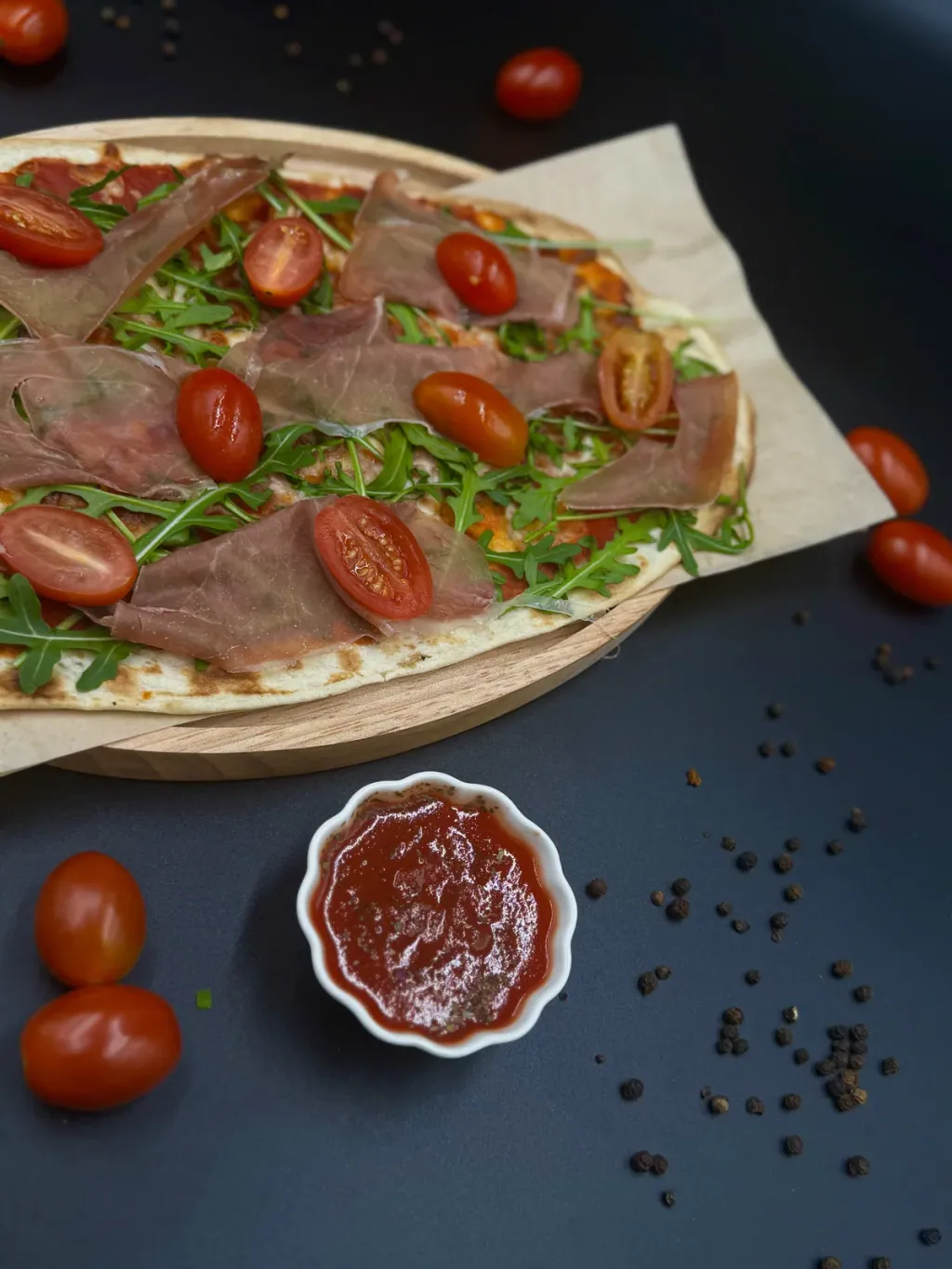 Podpłomyk z szynką parmeńską, rukolą i pomidorkami koktajlowymi na papierze do pieczenia